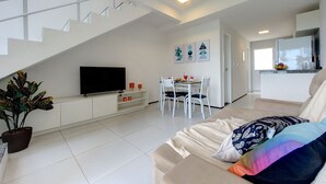 A modern living room with a staircase, a dining area, and a kitchen. - Triplex Hidromassagem em Porto das Dunas (Aquiraz)