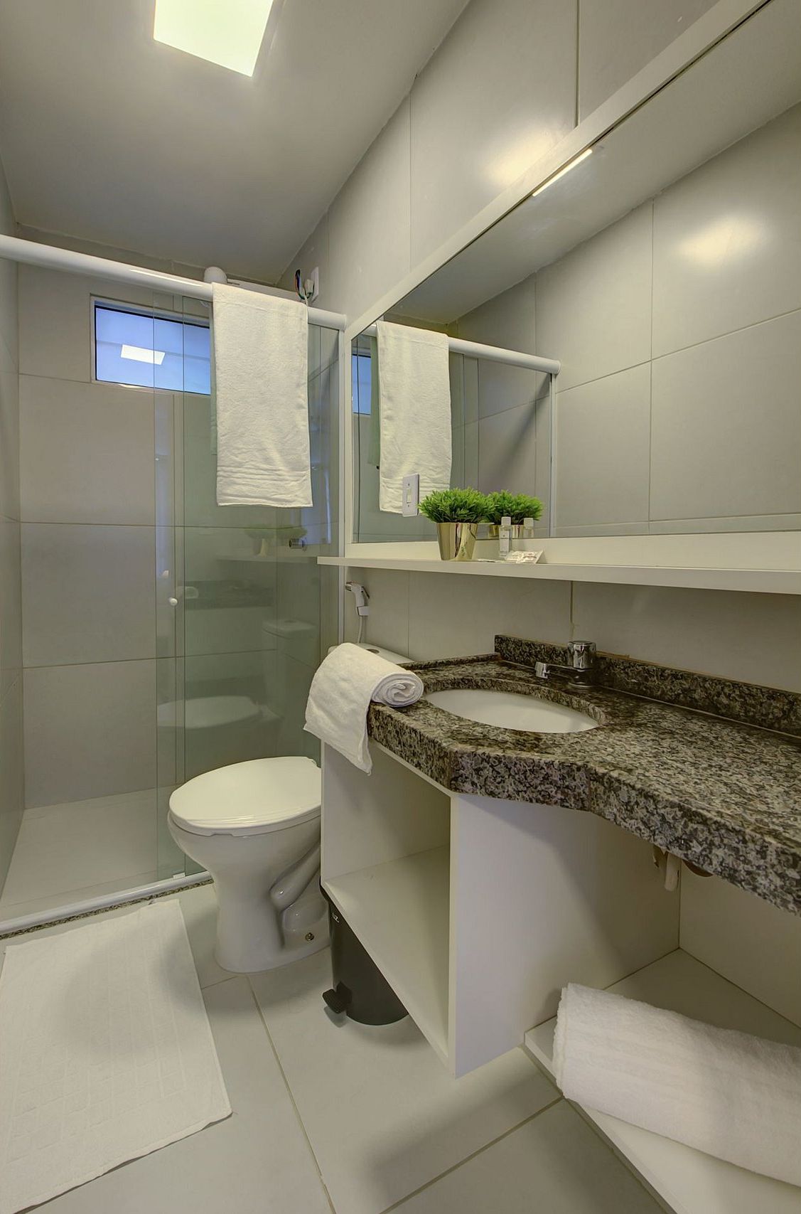 Un baño moderno con cabina de ducha de vidrio, inodoro, lavamanos con encimera de granito y espejo sobre el lavamanos.
