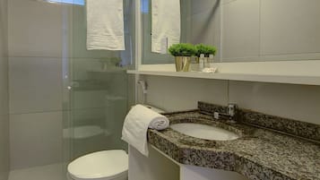 Un baño moderno con cabina de ducha de vidrio, inodoro, lavamanos con encimera de granito y espejo sobre el lavamanos.