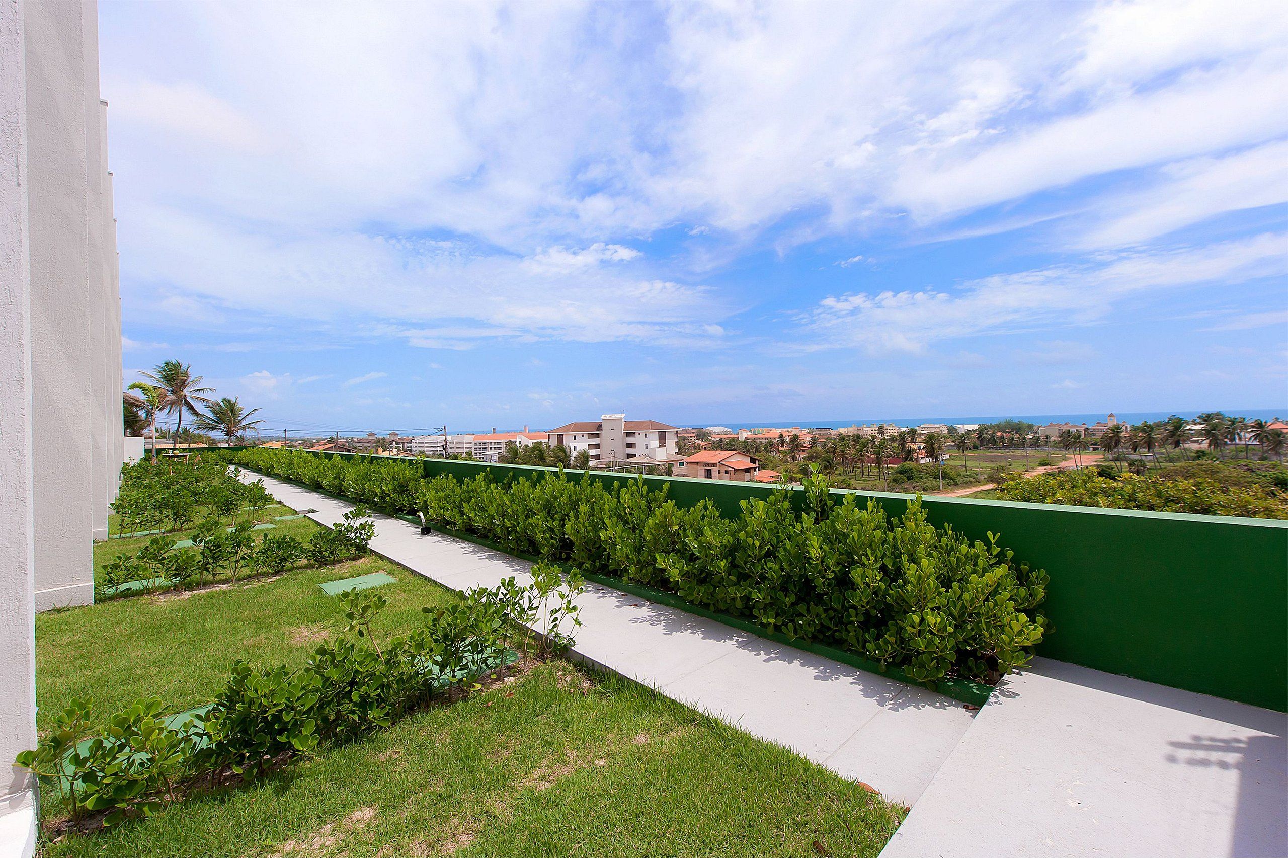 A balcony with a view of a coastal area, a green wall, and a pathway.