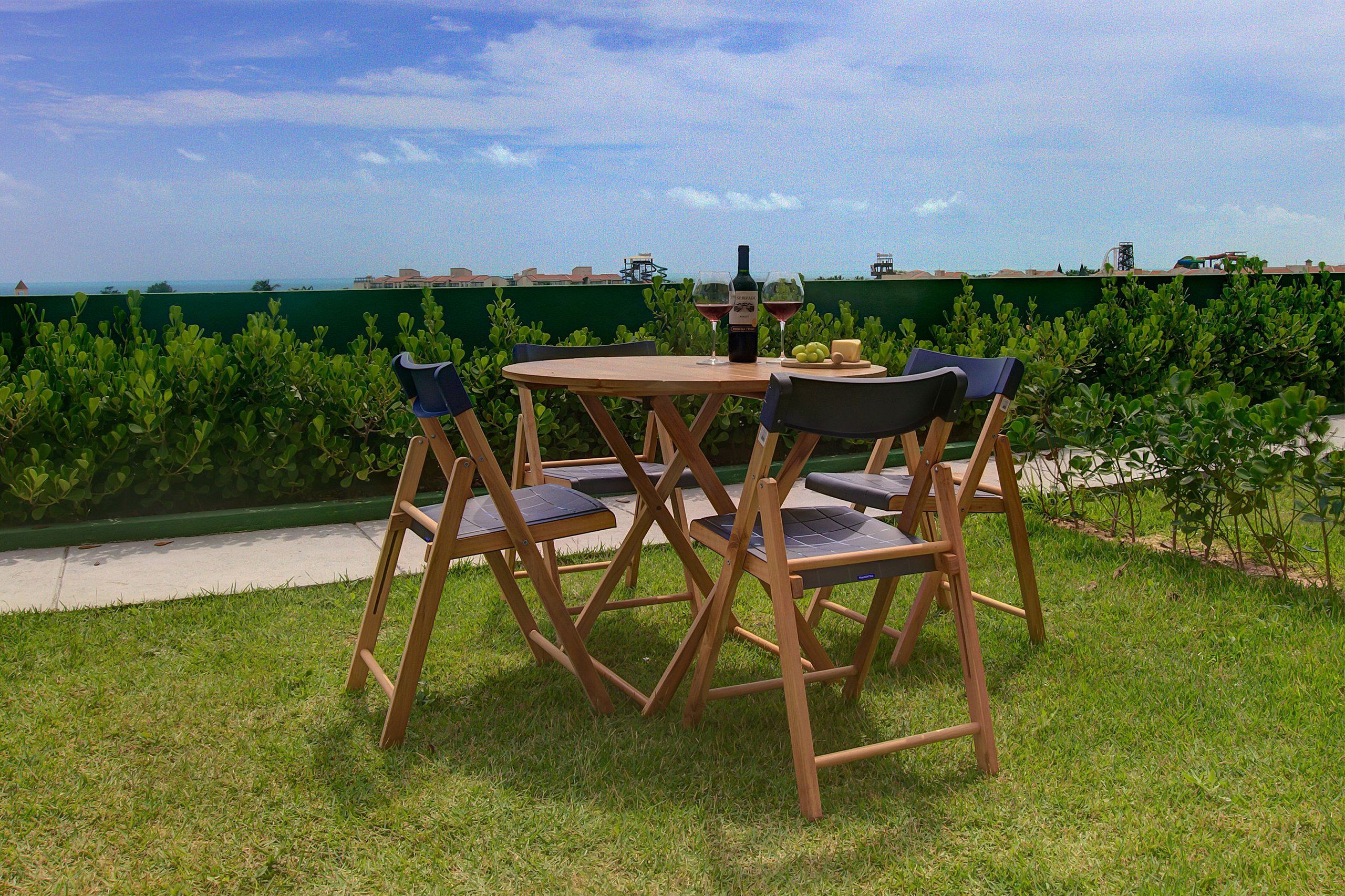 Un juego de mesa y sillas de madera al aire libre, con vista al mar y edificios al fondo.