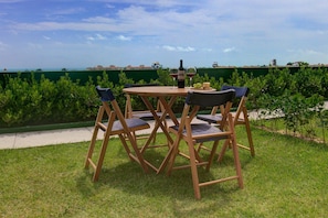 A wooden table and chairs set outdoors with a view of the sea and buildings in the background.