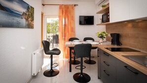 Cocina compacta con comedor, televisor montado sobre la encimera y vistas al exterior a través de una ventana.