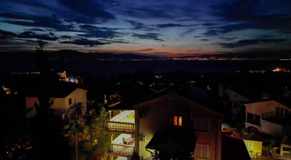 A nighttime view of a coastal area with buildings and a distant cityscape.
