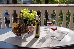 Ein Tisch mit einer Weinflasche, zwei Weingläsern, einer Obstschale und einem Blumenstrauß auf einem Balkon.