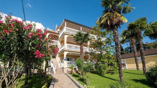 Un hotel de varios pisos con una escalera central, rodeado de exuberante vegetación y palmeras.