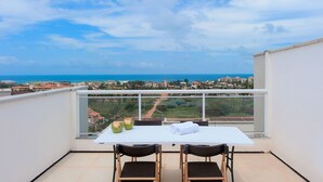 A balcony with a white table, two chairs, and a view of the sea and cityscape. - Chalé Família em Porto das Dunas (Aquiraz)