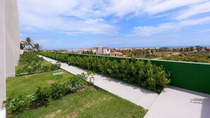 A balcony with a view of a coastal area, a green wall, and a pathway. - Chalé Família em Porto das Dunas (Aquiraz)