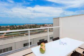 Un balcon avec une table blanche, deux noix de coco et une vue sur le paysage urbain de la côte.