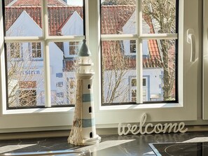 A room with a view of buildings through large windows, a decorative lighthouse, and a 'welcome' sign on the floor.