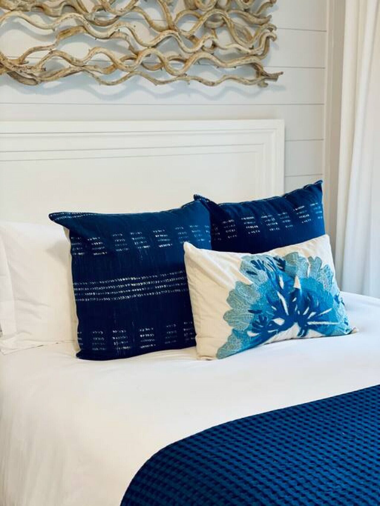 A bed with white bedding and two decorative pillows, one with text and the other with a blue floral design.