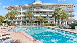 A hotel with a large pool, multiple balconies, and palm trees.