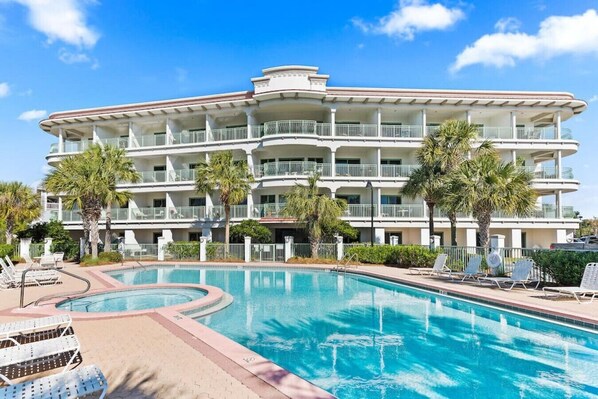 A hotel with a large pool, multiple balconies, and palm trees.