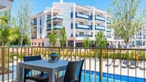 Een balkon met een zwembad, een wit en blauw gebouw op de achtergrond en bomen.