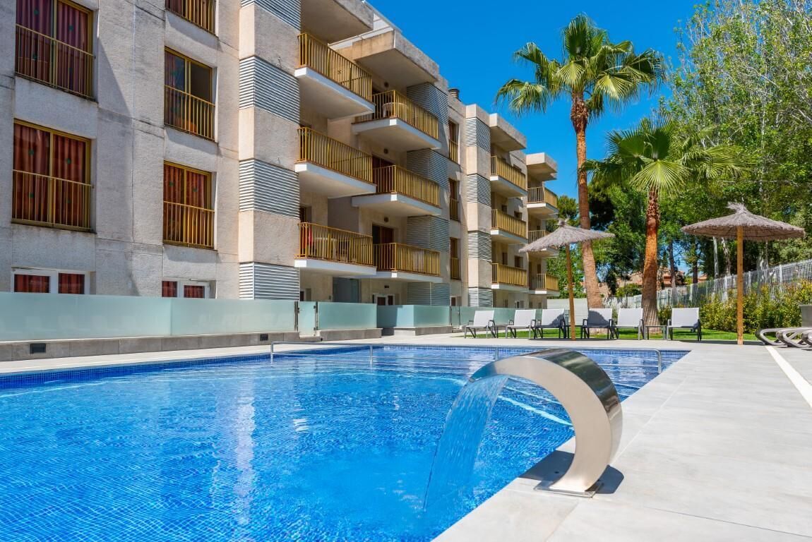 Un hôtel doté d’une piscine, d’un espace extérieur aménagé et de palmiers.