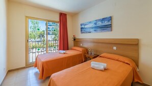 Een hotelkamer met twee bedden, een balkon met een rood gordijn en een schilderij van een zeegezicht.