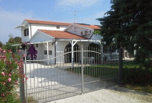 A two-story house with a red-tiled roof, a white exterior, and a gated entrance.