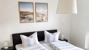 Een tweepersoonsbed met een gestreept dekbed, twee kussens, een nachtkastje met een lamp, en een wandlamp.