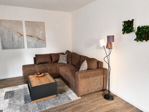 A modern living room with a sectional sofa, a wooden coffee table, a floor lamp, and abstract wall art. - "Big break" - Modern vacation apartment near Steinhude (Hagenburg)
