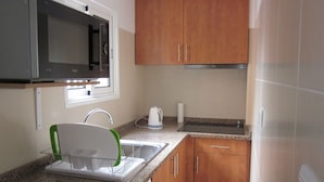 A compact kitchen with a microwave, sink, kettle, and wooden cabinets. - Apartment A  Rosy Apartments (Madeira)