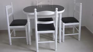 A dining area with a round table and four white chairs with black cushions. A painting of fruits and a bottle hangs on the wall above the table. - Apartment A  Rosy Apartments (Madeira)