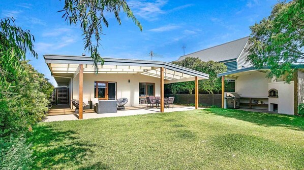 A modern house with a covered patio, a barbecue area, and a well-maintained lawn.