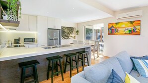 Une cuisine moderne avec des meubles blancs, un réfrigérateur en acier inoxydable et un coin bar équipé de tabourets.
