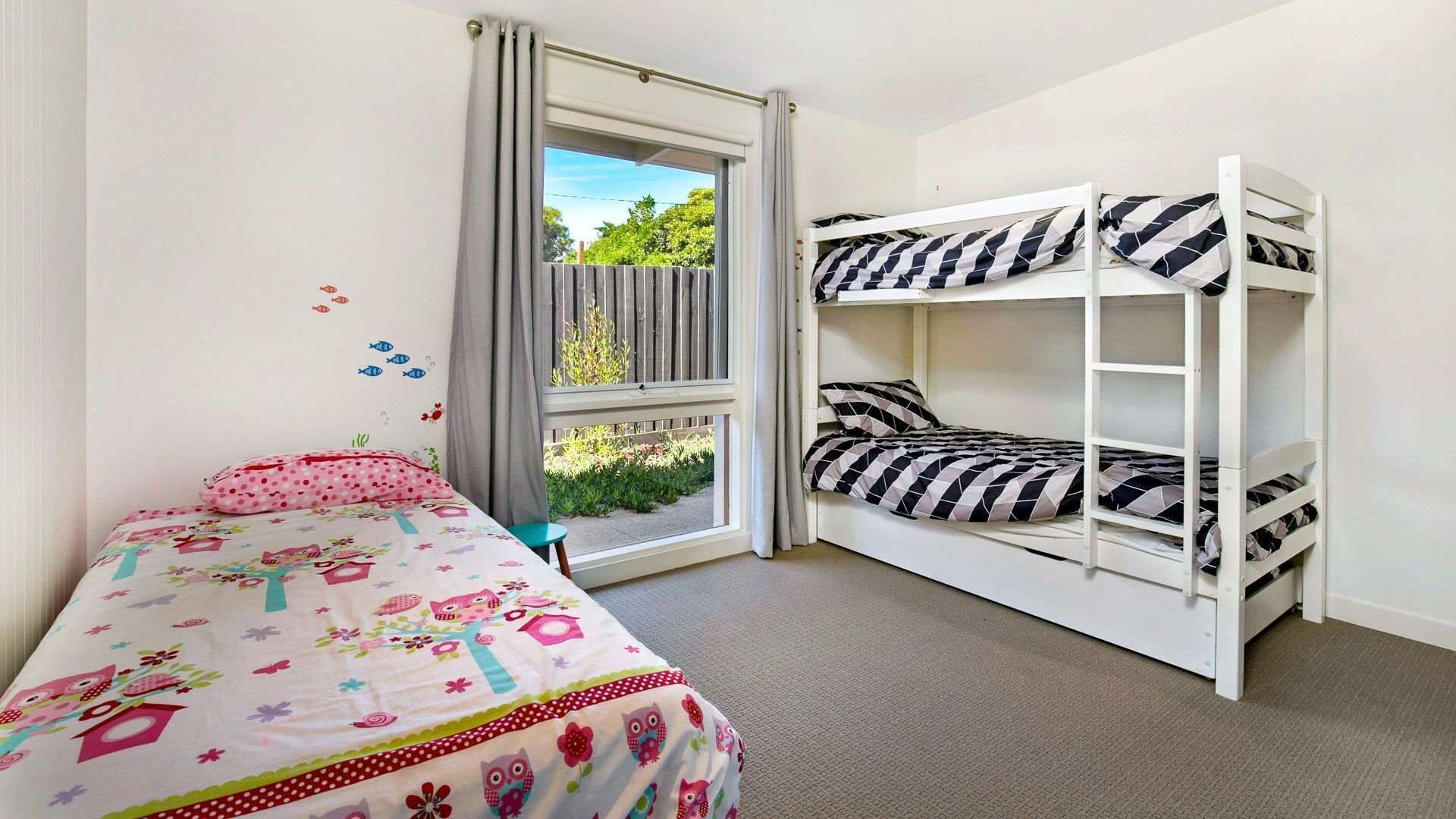 Een slaapkamer met een enkel bed, een stapelbed, een raam met gordijnen en uitzicht op groen.