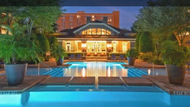 Un hotel con piscina, una zona techada con asientos y un edificio de varios pisos.
