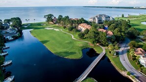 An aerial view of a golf course with a water body, a bridge, and residential buildings.