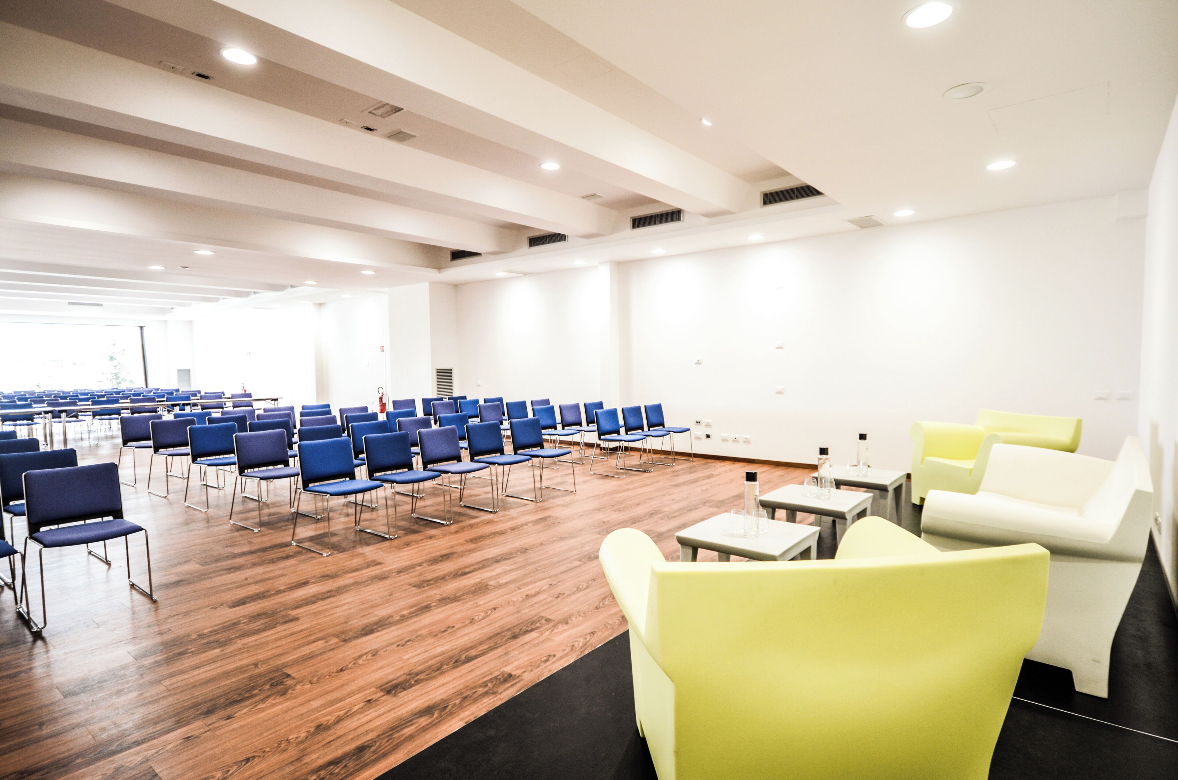A conference room with rows of chairs, a stage, and seating areas with tables and chairs.