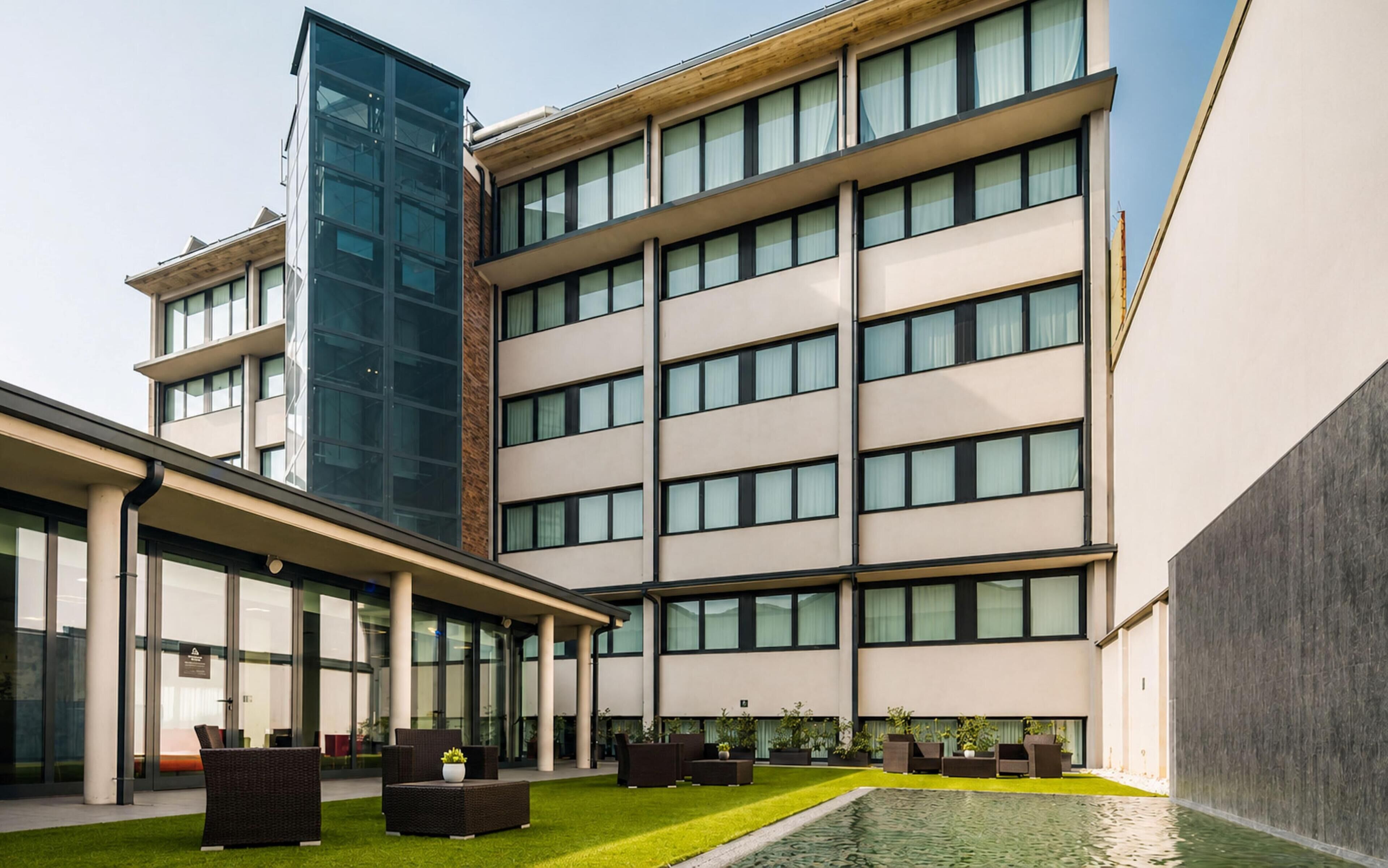 Un edificio moderno con varios pisos, ventanas amplias y un patio con asientos al aire libre.