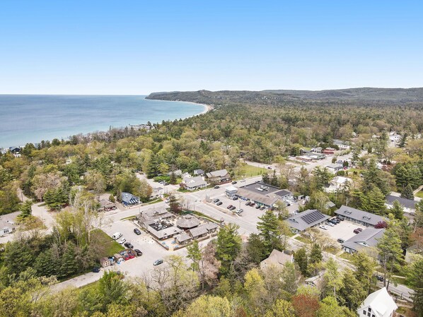 An aerial view of a coastal town with a mix of residential and commercial buildings, a parking lot, and a beach visible in the background.