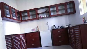 A compact kitchen with dark wooden cabinets, a white refrigerator, and a gas stove. - Mapembeani (Zanzibar)