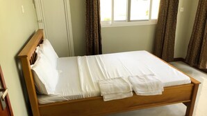 A neatly made bed with white linens and towels, a wooden headboard, and a window with curtains. - Mapembeani (Zanzibar)