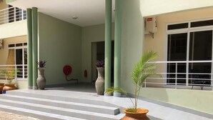 A building entrance with steps leading up to a door, large green pillars, and potted plants. - Mapembeani (Zanzibar)
