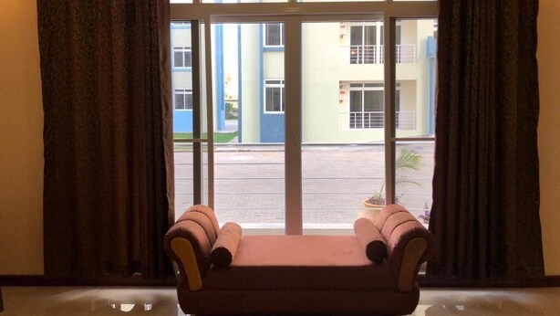 A room with a sofa facing a large window with curtains, a view of a building outside. - Mapembeani (Zanzibar)