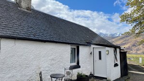 A white house with a grey roof, a door, and a small patio with a table and chairs. - 3 bedroom accommodation in Corran, near Arnisdale (Corran, near Arnisdale)