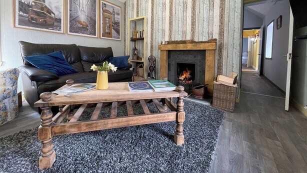 A living room with a fireplace, a sofa, and a coffee table. There are framed pictures on the wall and a bookshelf. - 3 bedroom accommodation in Corran, near Arnisdale (Corran, near Arnisdale)
