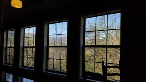 Habitació amb tres grans finestres que donen vista a arbres i muntanyes.