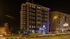 Monikerroksinen hotelli, jonka julkisivussa on suuri, huomiota herättävä kyltti, jossa lukee ”Real House”, hyvin valaistu sisäänkäynti ja useita autoja sisältävä pysäköintialue.