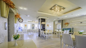 A hotel dining area with multiple tables and chairs, a large chandelier, and a clock on the wall. - Real House Boutique Hotel (Kocasinan)