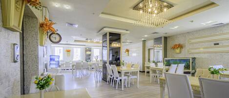 Un comedor de hotel con varias mesas y sillas, un gran candelabro y un reloj en la pared.