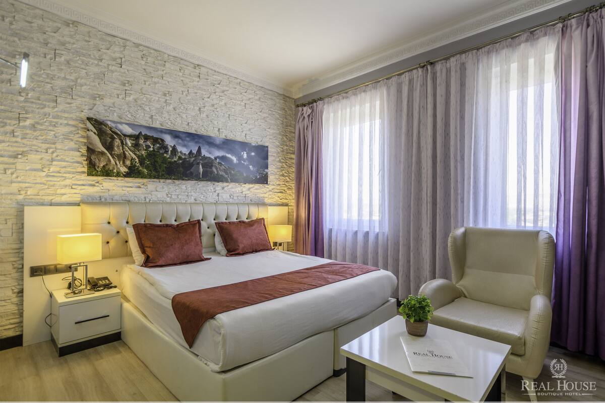 Ein Hotelzimmer mit einem großen Bett, einem Nachttisch mit Lampe, einem Sessel und einem Tisch mit Pflanze.
