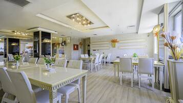 A hotel dining area with multiple tables and chairs, a chandelier, and decorative wall elements.