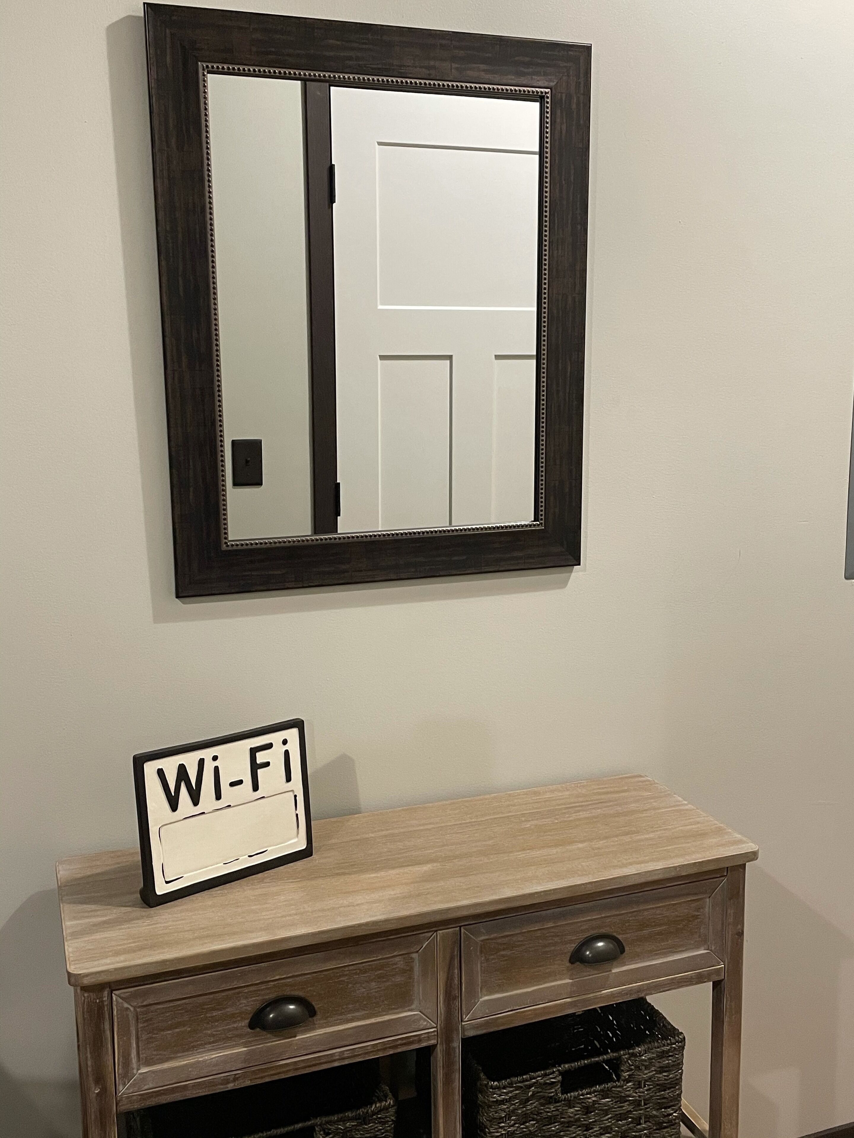 A mirror with a dark frame, a small sign reading "Wi-Fi", and a wooden dresser below it.