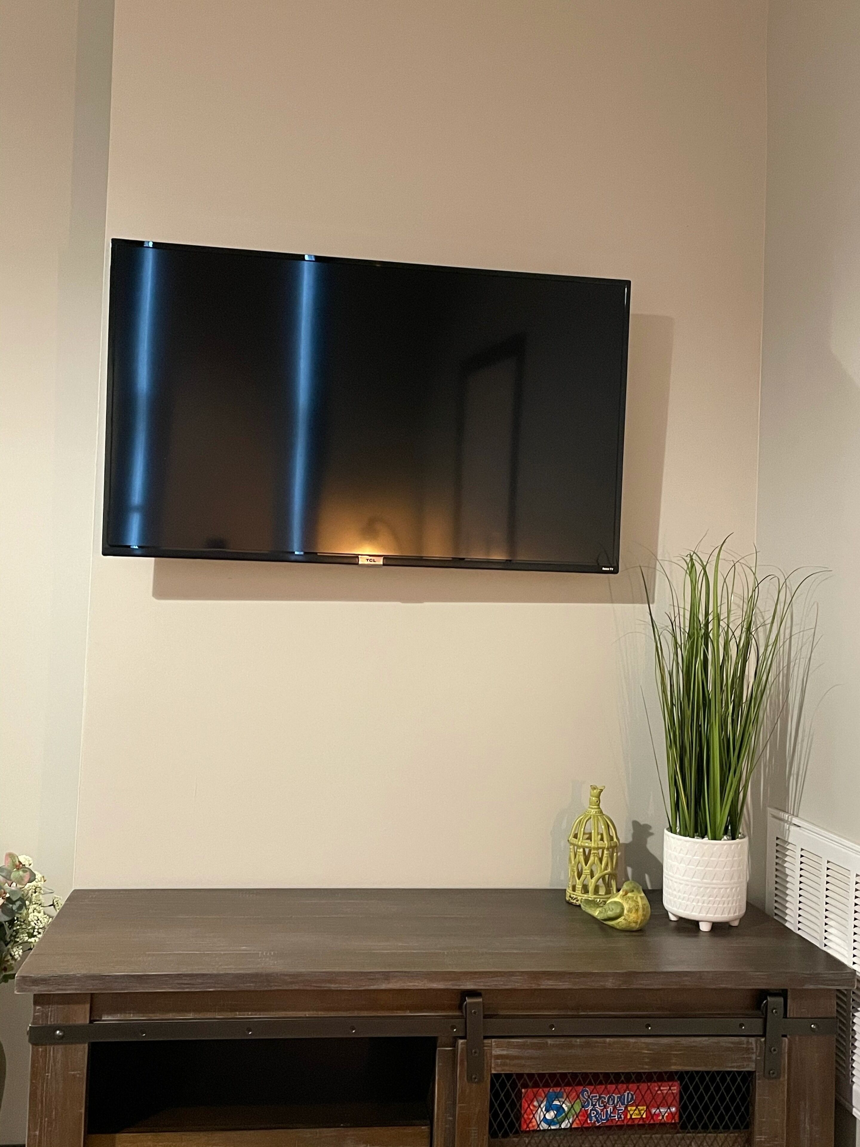 A flat-screen TV mounted on a wall above a wooden entertainment center with a potted plant and a decorative item.