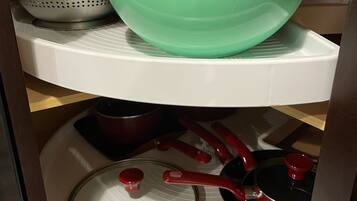 Una cocina con un bol verde en el estante superior y varias ollas y sartenes en el inferior.