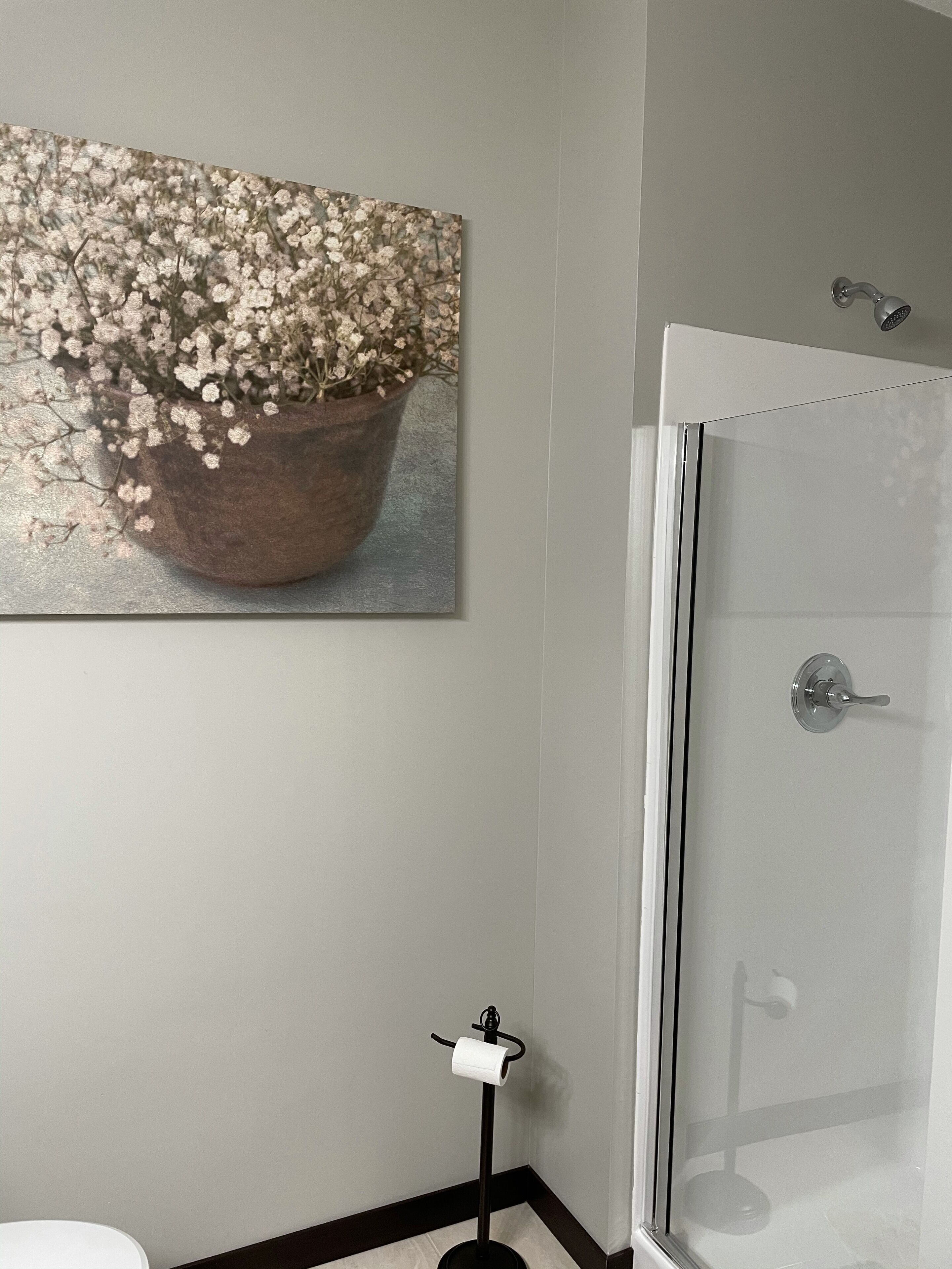 Un baño con ducha, inodoro y un cuadro de flores en la pared.