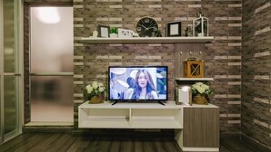 Uma sala de estar moderna com uma TV de tela plana sobre um móvel branco, uma parede com padrão de tijolos e um armário de madeira.